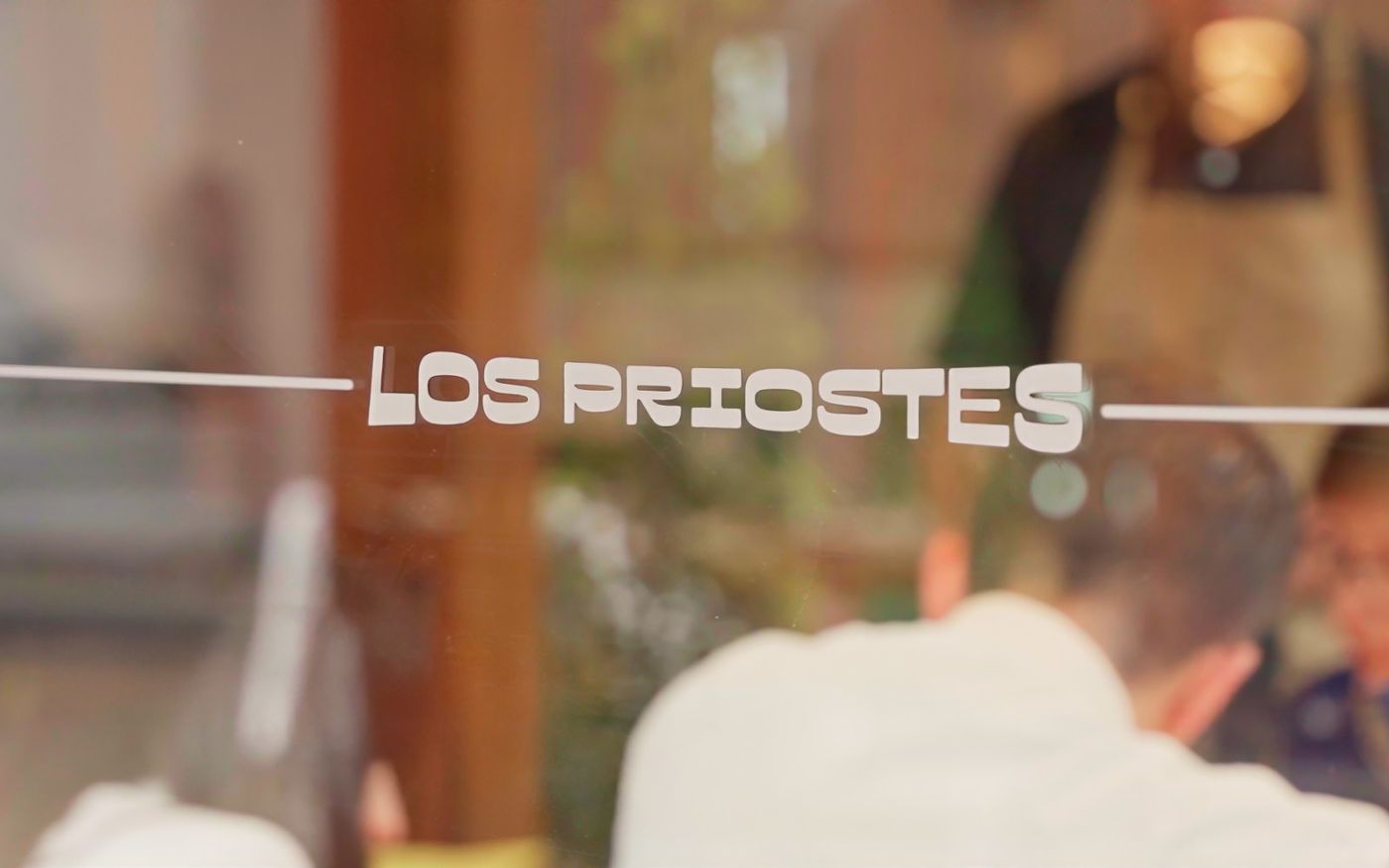 Nombre de Los Priostes grabado en el cristal de la ventana del restaurante, con el comedor reflejado al fondo
